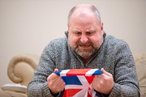 Harry Ward in rehearsals, grimacing as he holds up a Union flag. 